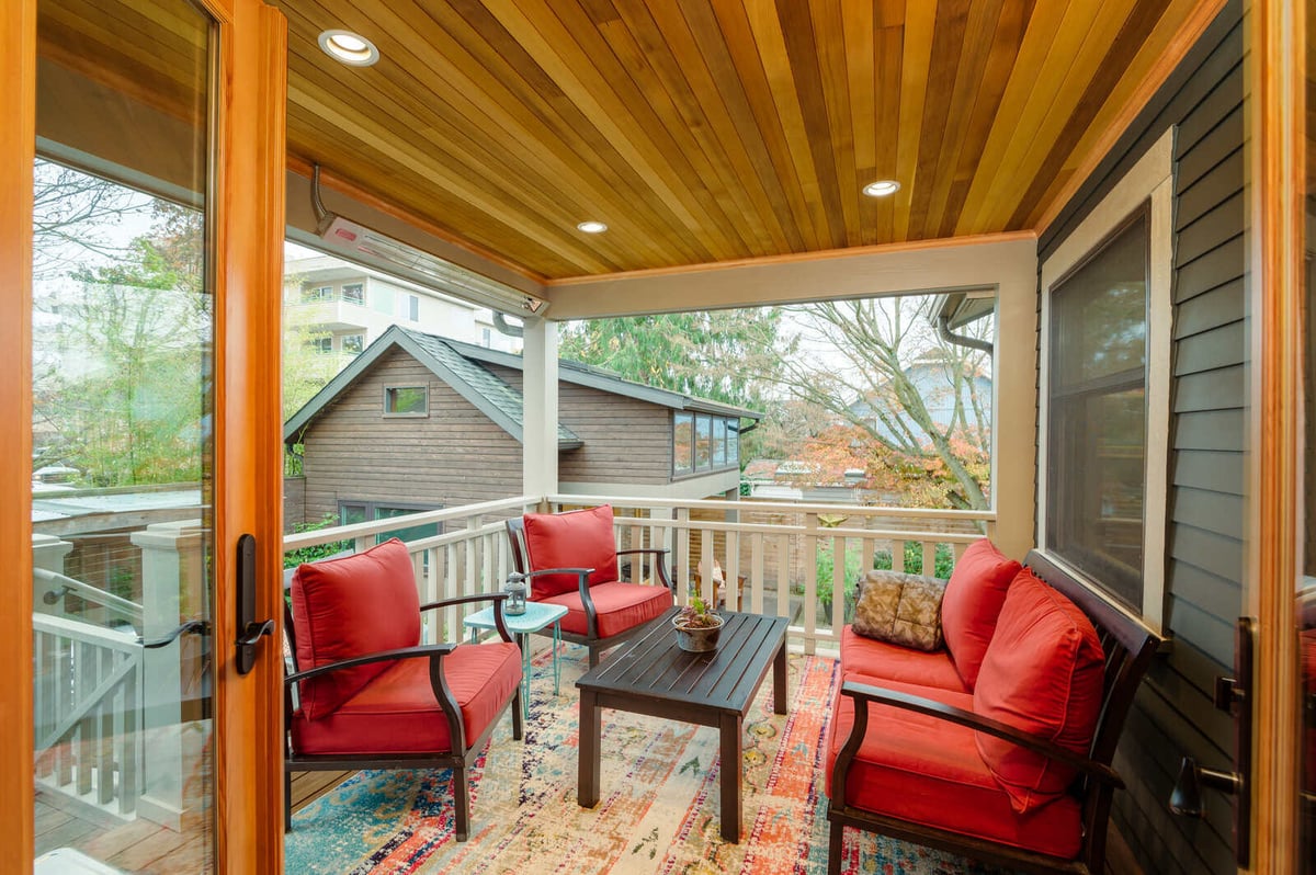 Covered outdoor deck with wooden ceiling and cozy seating area by CB Construction in Seattle