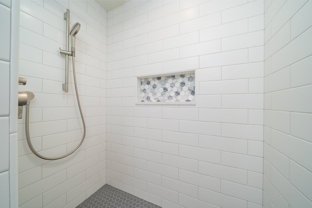 White subway tile shower with a modern shower head and niche by CB Construction in Seattle