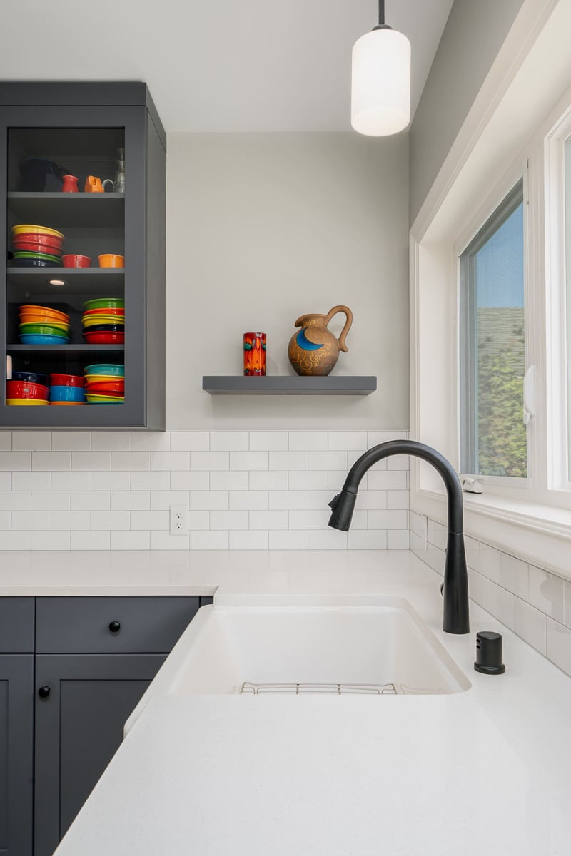 Bright kitchen by CB Construction in Seattle featuring grey cabinets, white countertops, and colorful dishware