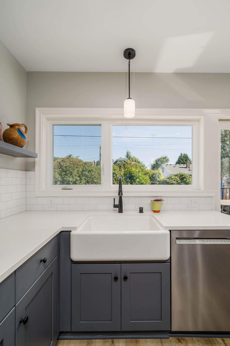 Bright kitchen renovation in Seattle by CB Construction featuring a white farmhouse sink, large windows, and grey cabinets