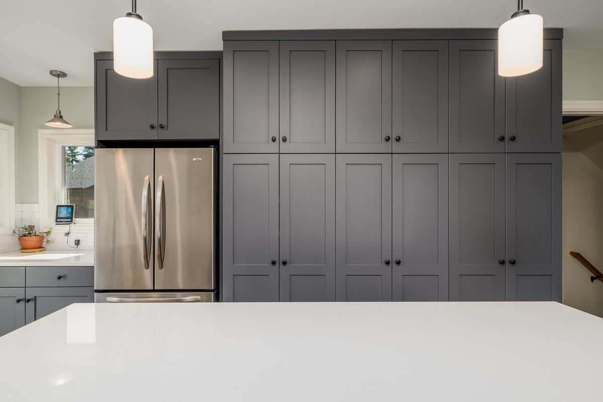 Modern kitchen remodel in Seattle by CB Construction with grey cabinets, a stainless steel fridge, and pendant lighting