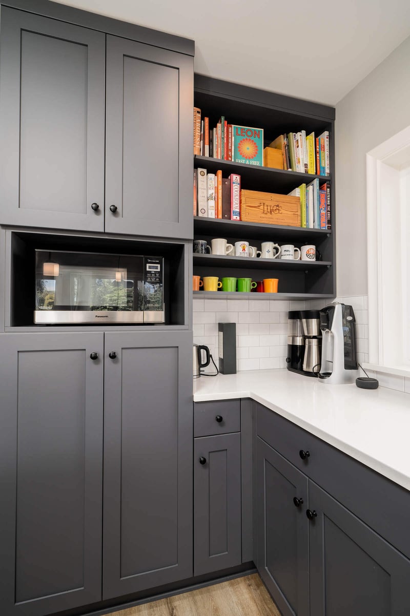 Seattle kitchen remodel by CB Construction featuring grey cabinetry, a built-in microwave, and colorful mugs displayed on open shelves
