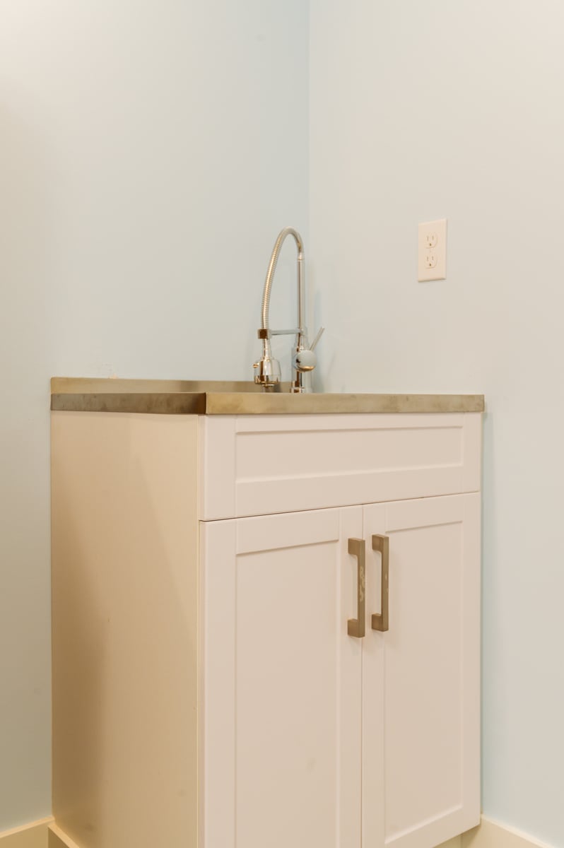 Laundry room featuring white cabinetry and stainless steel sink in a remodeled Seattle basement, by CB Construction