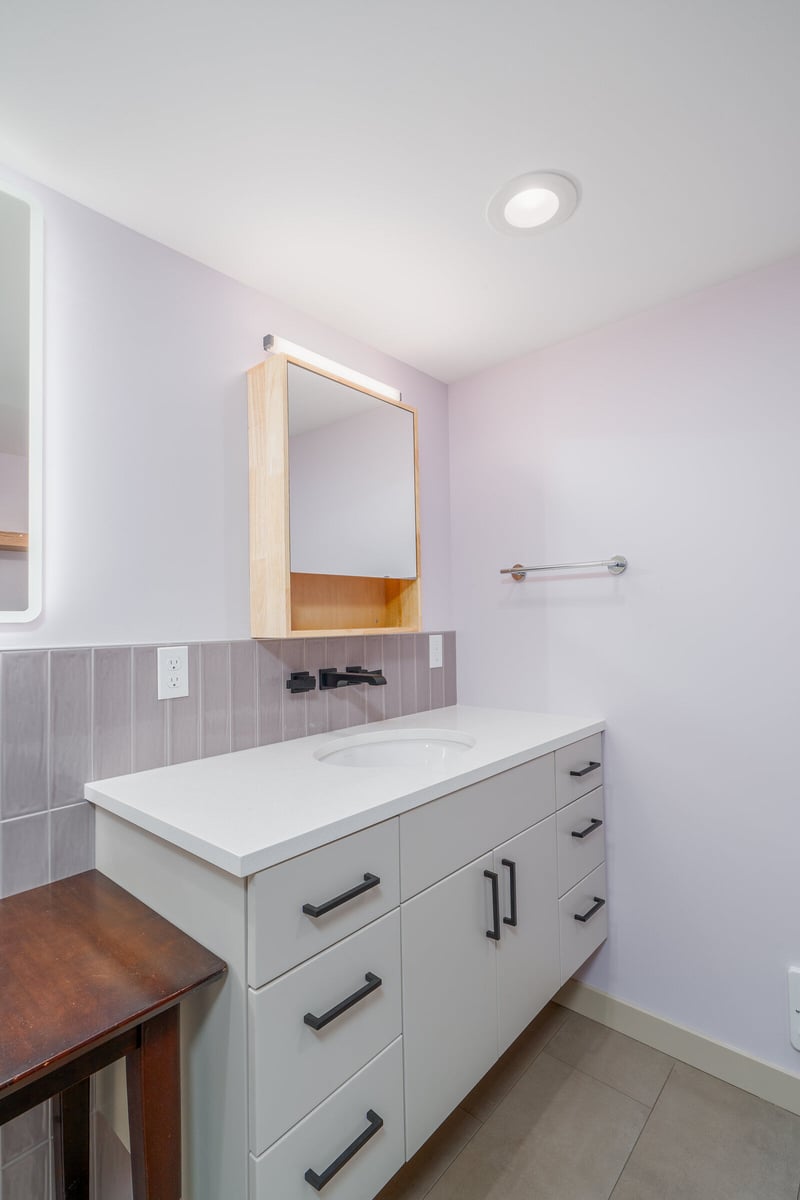 A modern bathroom vanity with white countertop and wooden framed mirror in a basement ADU remodel by CB Construction in Seattle