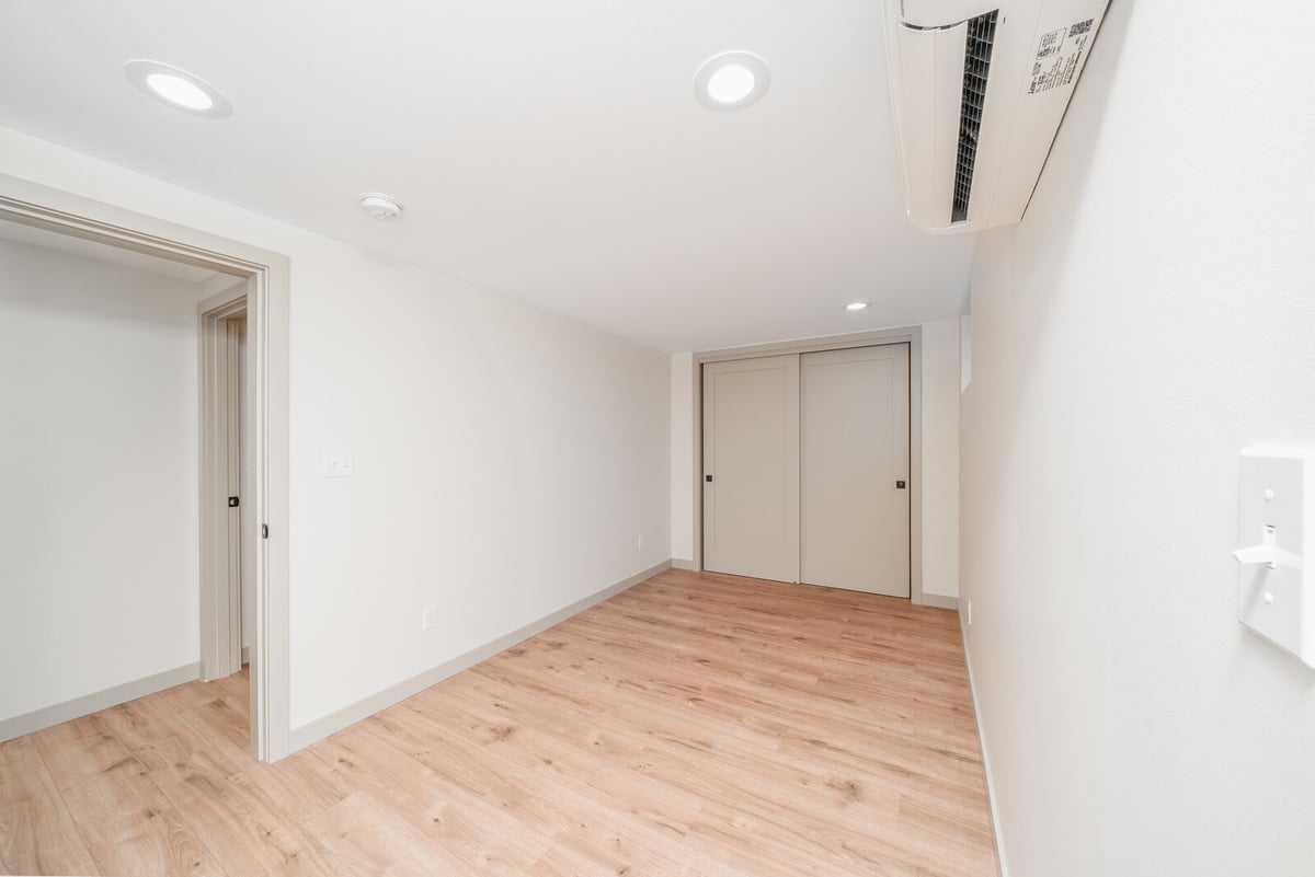 Basement room with light wood flooring and modern air conditioning unit in Seattle ADU by CB Construction