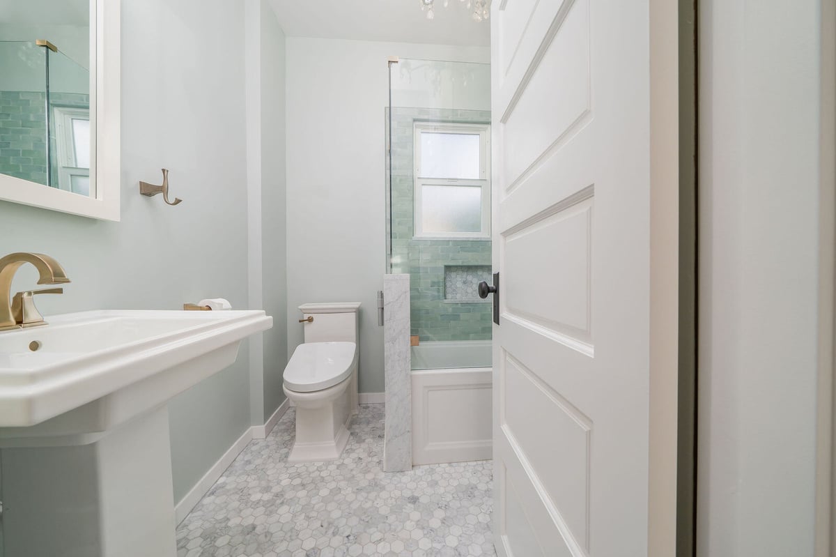 Bathroom with white pedestal sink, toilet, and glass shower featuring green subway tiles, remodeled by CB Construction in Seattle