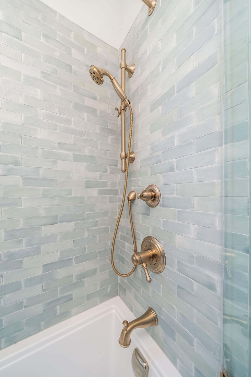 Close-up of brass shower fixtures on green subway tile in a bathroom remodel by CB Construction, Seattle