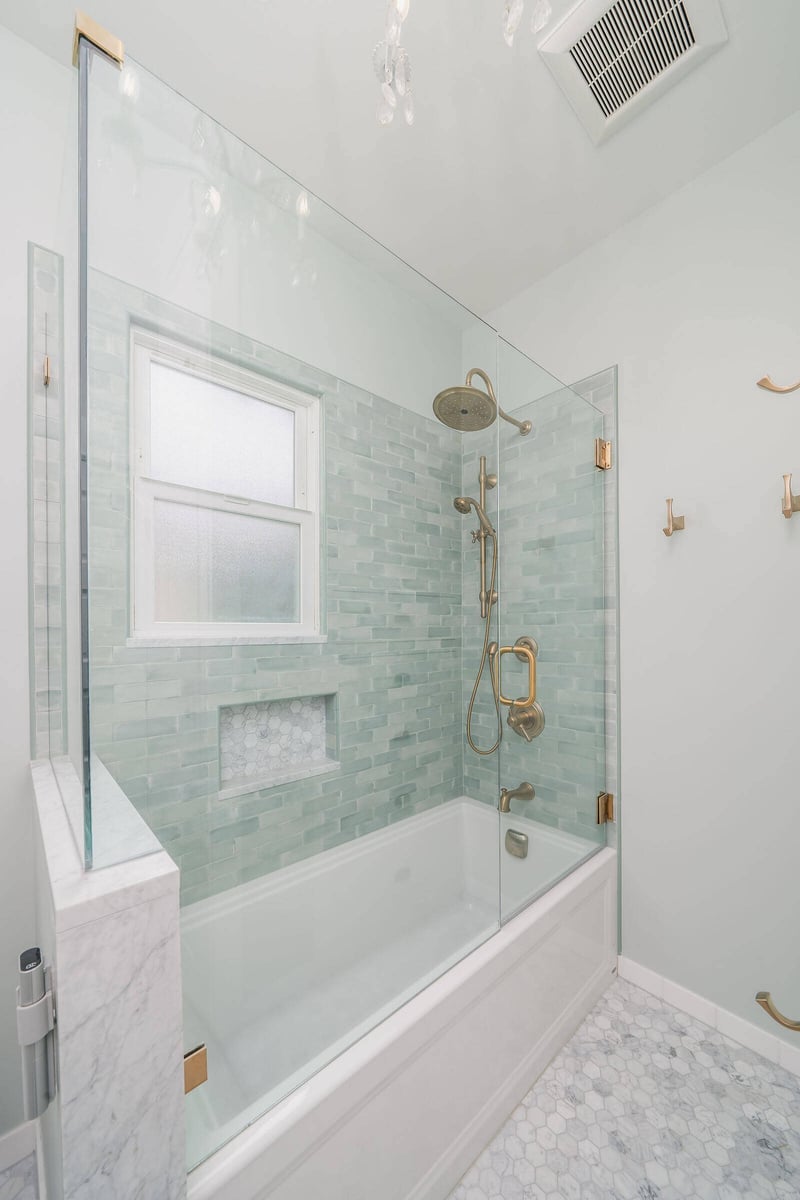 Green tiled shower with brass showerhead and frosted window in a bathroom remodel by CB Construction in Seattle